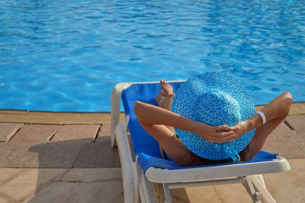 woman in blue hat lounging by pool